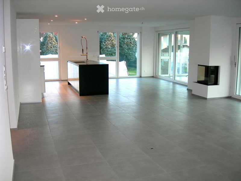 Empty room with tiled floor, white walls, large windows, and a kitchen island with a sink and faucet.