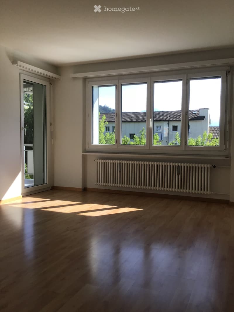 Empty room with wooden flooring, large windows, and a radiator. No furniture or equipment present.