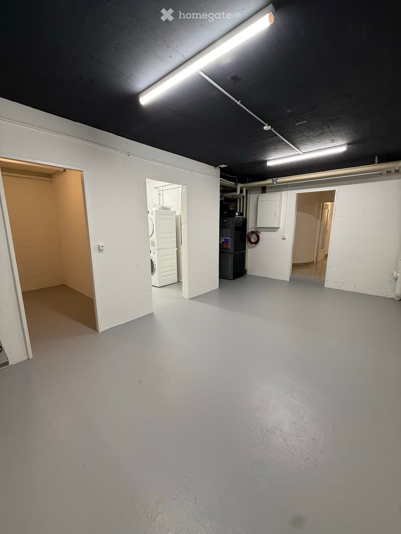 Empty room with grey concrete floor and white walls, featuring a private washing machine in the background.