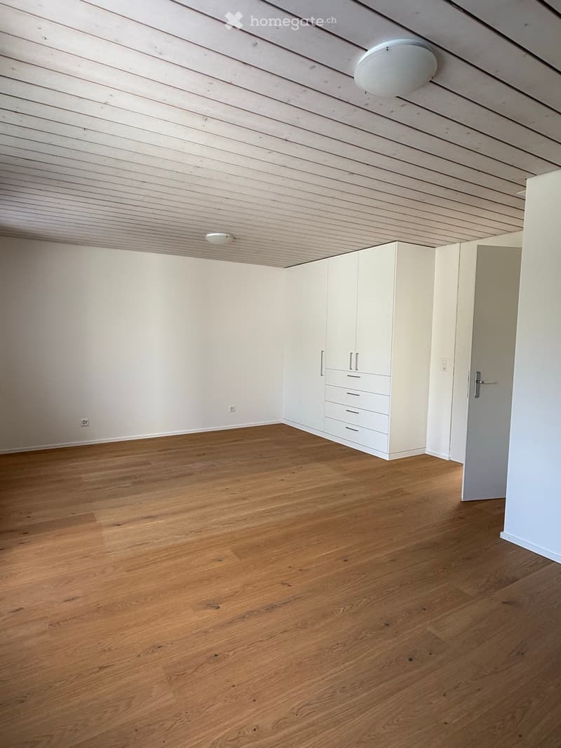 Empty room with light wooden flooring, white walls, and built-in white cabinetry with drawers and doors.