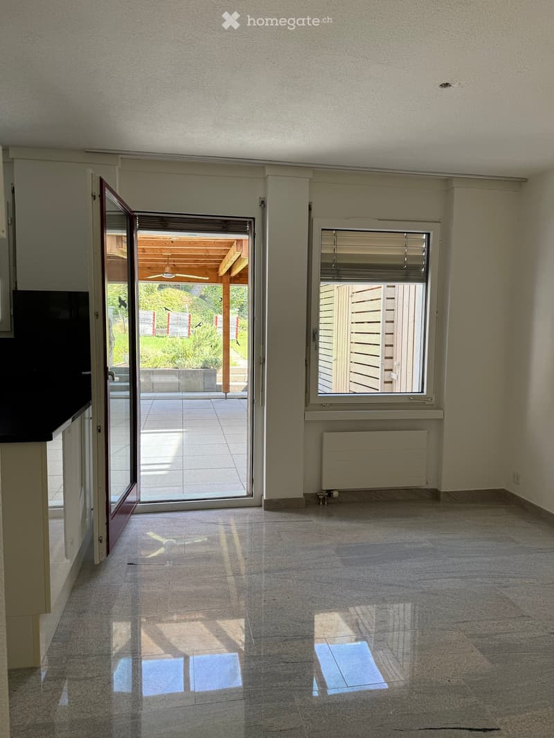 Empty room with tiled floor, large sliding glass door leading to a patio, window with blinds, radiator, and visible sunlight shadows.