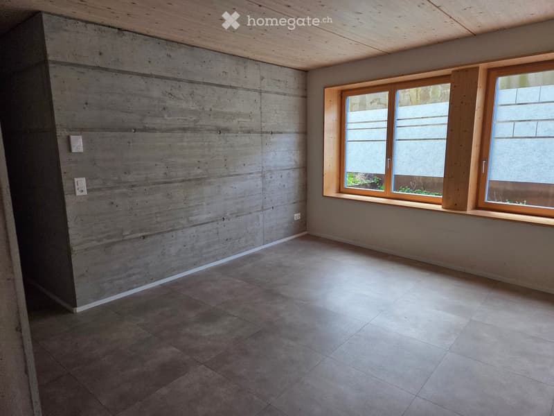 Empty room with concrete walls, tiled floor, and large wooden-framed windows allowing natural light.