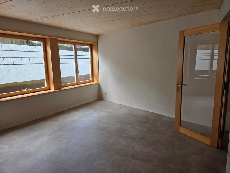 Empty room with tiled floor, light-colored walls, large windows with wooden frames, and a glass door leading to another space.
