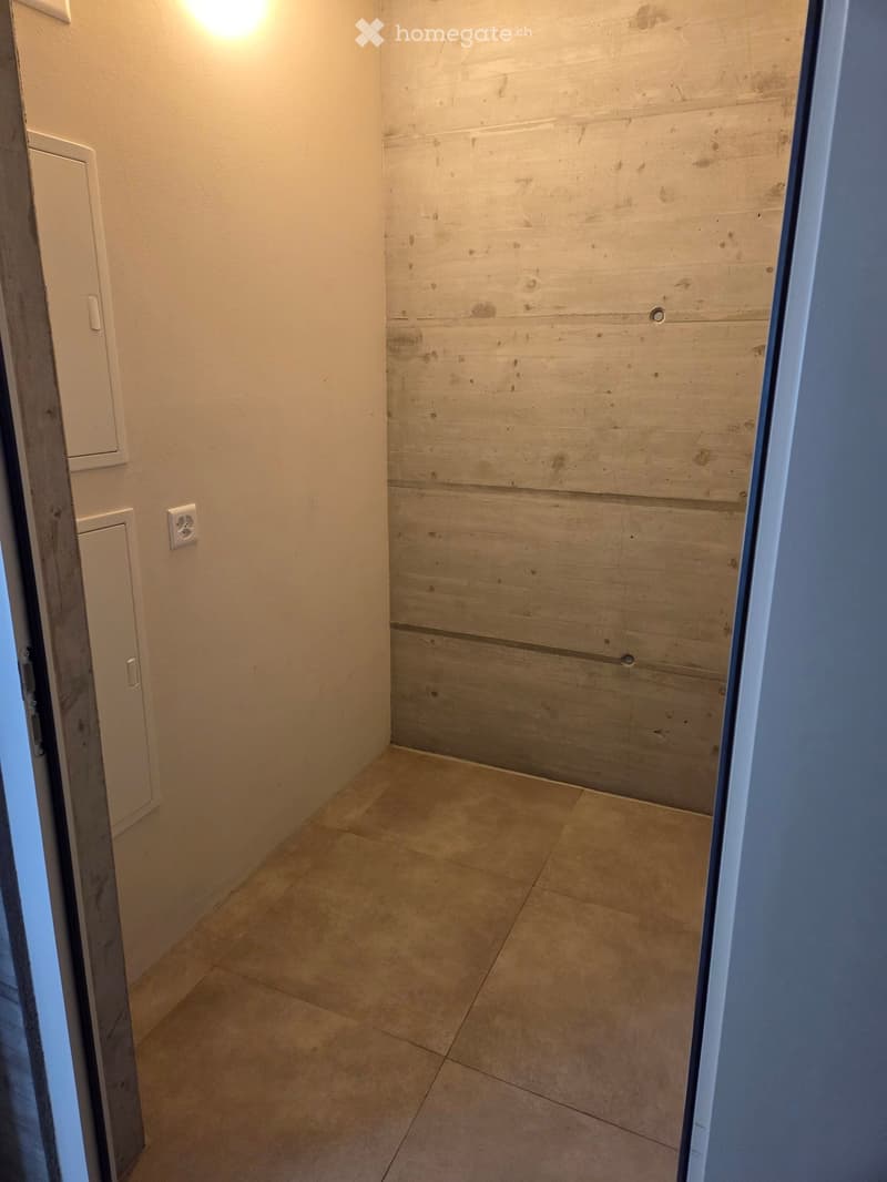 Empty hallway with beige tiled floor, white walls, and a light switch visible on the left wall.
