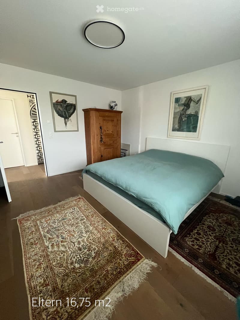 Bedroom with a bed, wardrobe, mirror, and two picture frames on the wall. The room features wooden flooring and two patterned rugs.