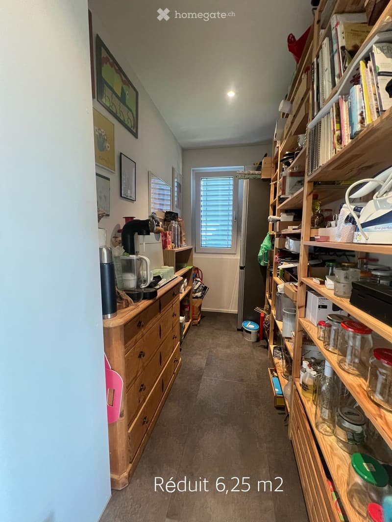 A narrow hallway with wooden shelves on the right side, a small wooden cabinet on the left, and a door leading to another room at the end.