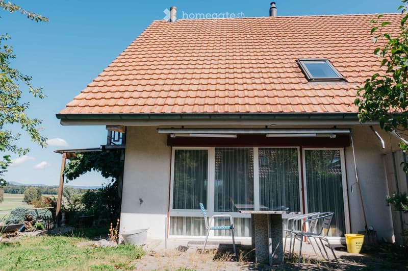 Single-story house with a tiled roof, large windows, and a covered patio area with outdoor furniture.