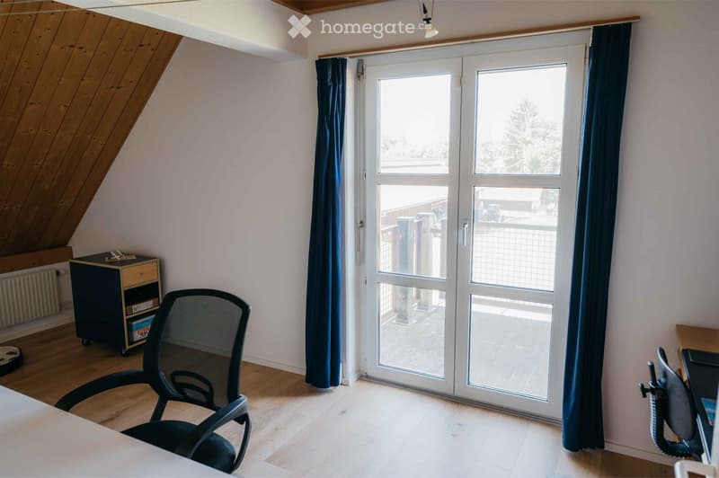 Bright room with wooden flooring, large sliding glass doors leading to a balcony, two chairs, a small cabinet, and a curtain.