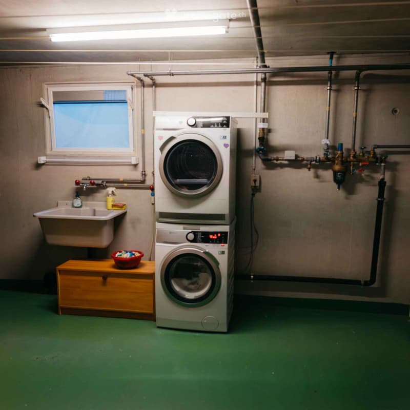Utility room with a washing machine, sink, and small wooden stool holding a bowl.