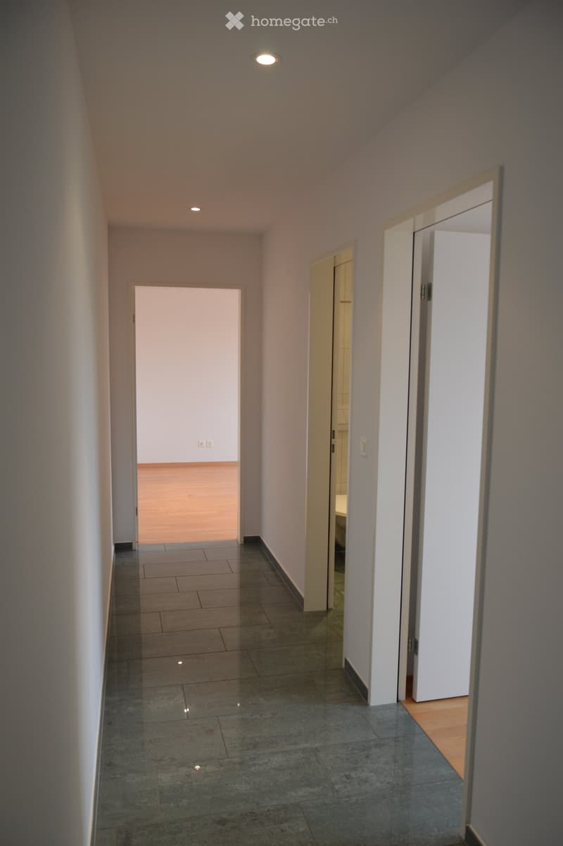 Empty hallway with tiled floor, white walls, and recessed lighting. Three doors lead to other rooms.