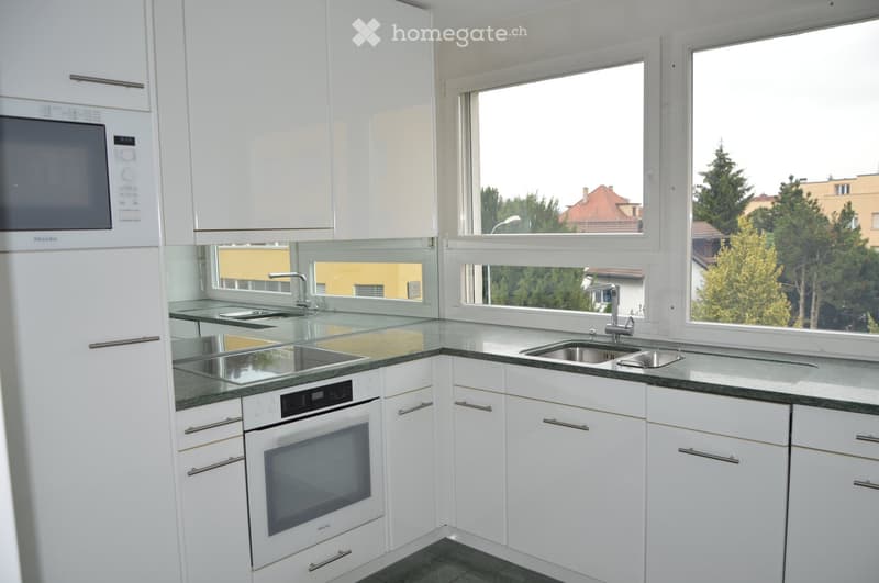 Modern kitchen with white cabinets, stainless steel appliances, and large windows offering a view of the outside.