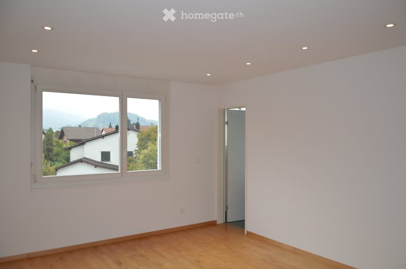 Empty room with light-colored walls, wooden flooring, and large windows offering a scenic view of the surrounding area.