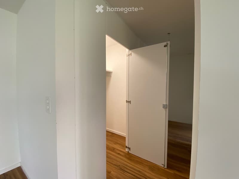 Empty hallway with white walls, wooden flooring, and a partially open door leading to another room.