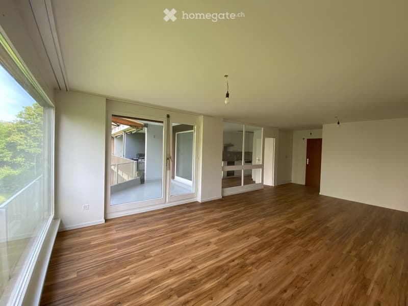 Empty room with wooden flooring, large windows, and sliding glass doors leading to a balcony area.