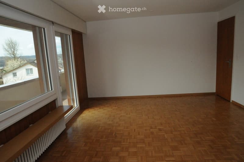 Empty room with wooden parquet flooring, large windows, and a wooden door. No furniture or equipment present.