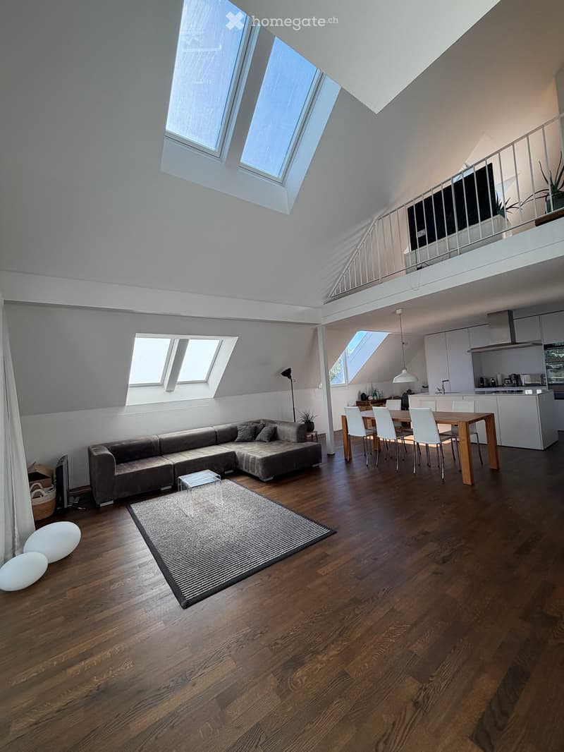Open-concept living and dining area with wooden flooring, skylights, a sectional sofa, coffee table, dining table with chairs, and a modern kitchen area.