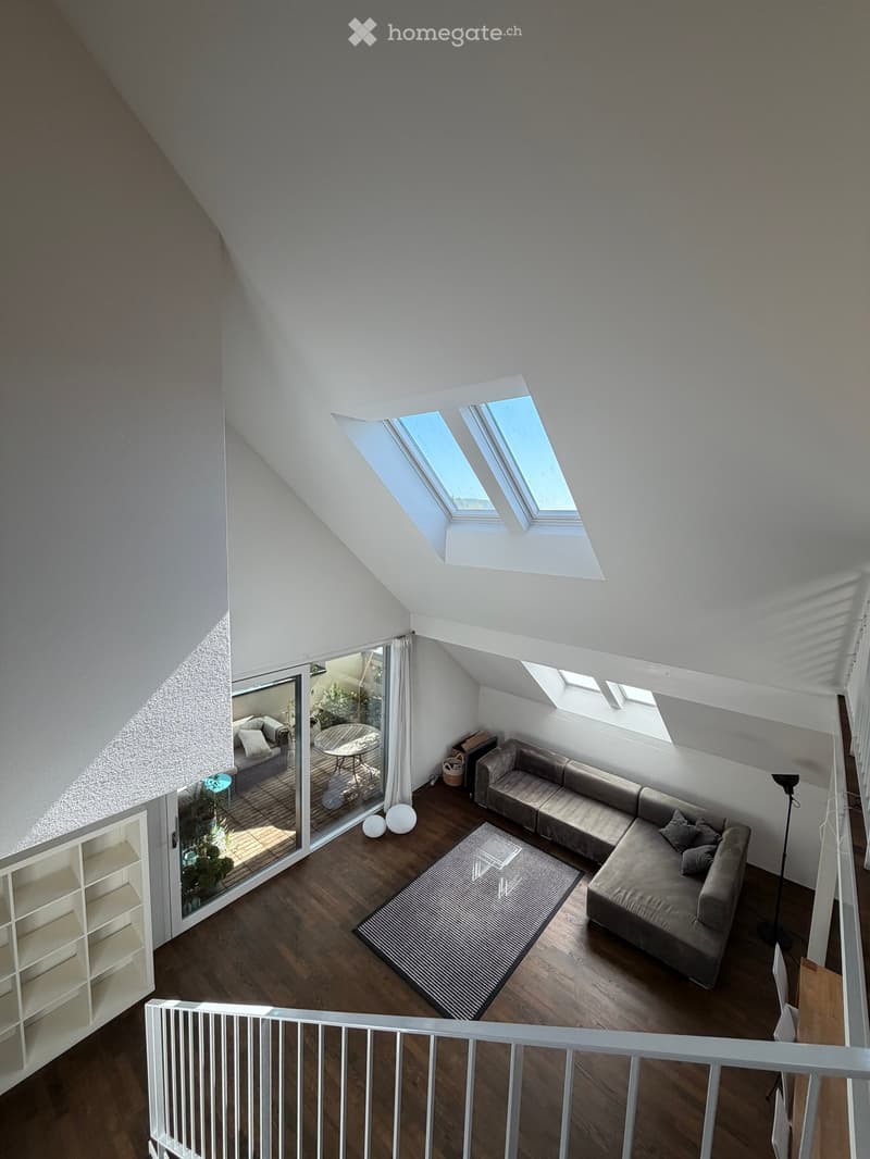 A modern living room with wooden flooring, a large sectional sofa, a coffee table, a round table, and a view of a balcony area with outdoor furniture.