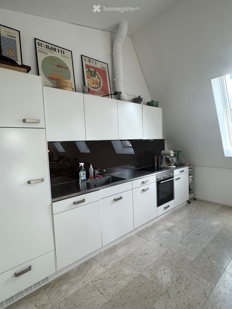 Modern kitchen with white cabinets, stainless steel appliances, marble flooring, and framed posters on the wall.