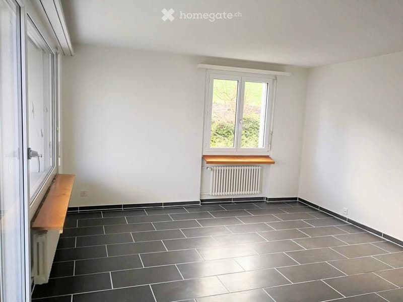 Empty room with grey tiled floor, white walls, two windows, and built-in wooden benches.