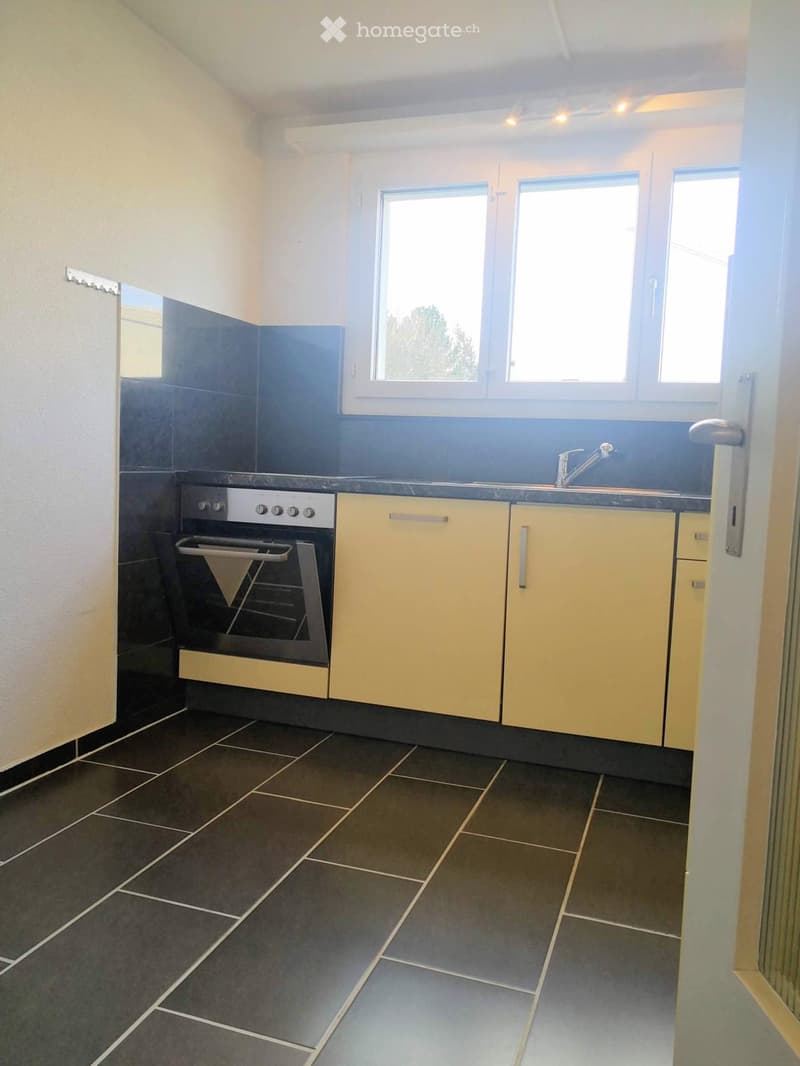 Modern kitchen with dark tiled floor, light yellow cabinets, stainless steel oven, and sink with faucet.