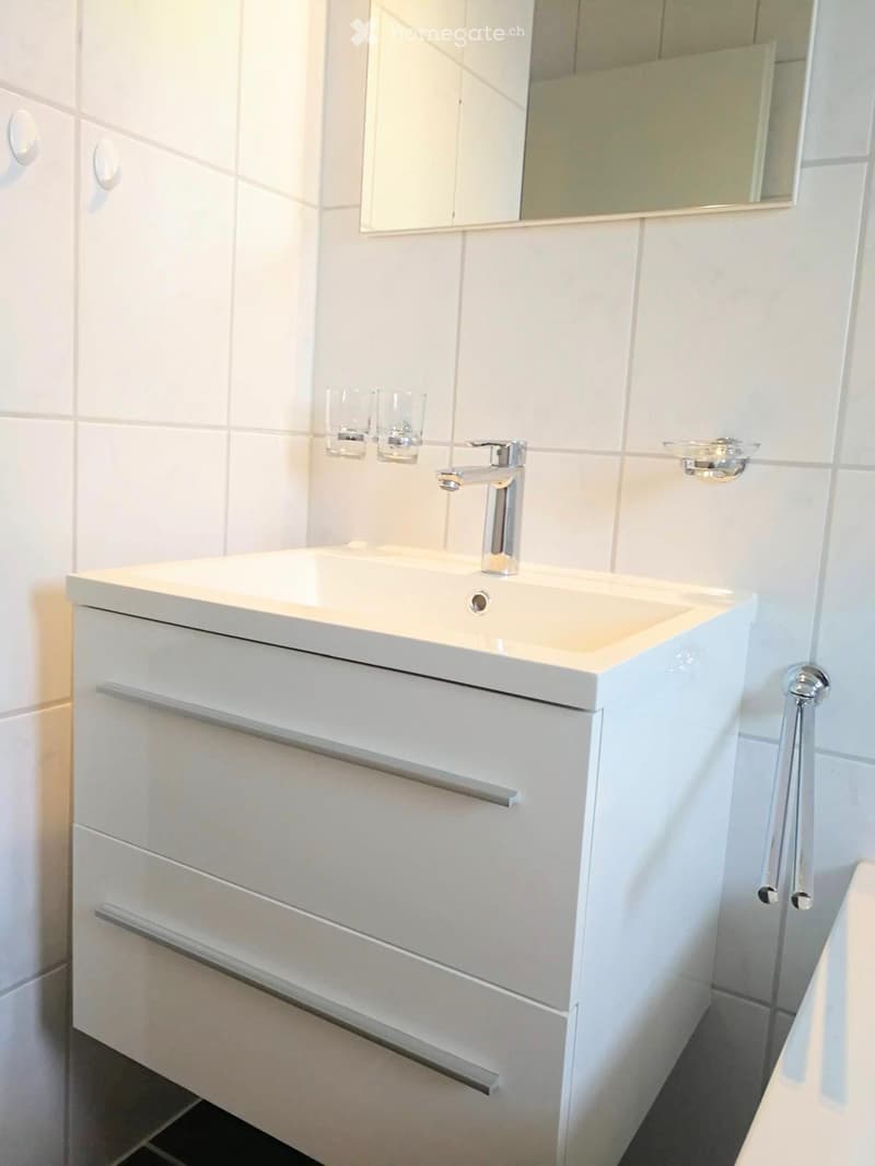 Modern bathroom with a white sink, chrome faucet, and mirrored cabinet above. Two small glass cups are placed on the countertop.