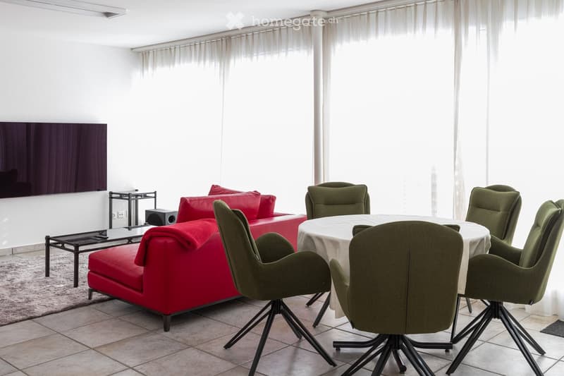 Modern living and dining area with a red sofa, a white dining table with green chairs, a large screen, and a small side table.
