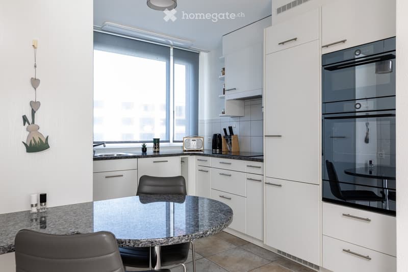 Modern kitchen with white cabinets, granite countertops, a round dining table with black chairs, and various appliances including an oven and a sink.