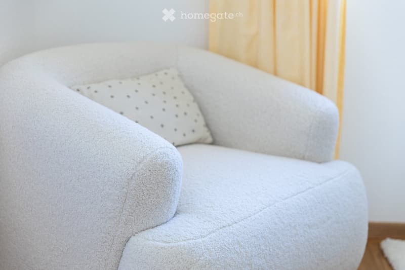 A light grey, plush sofa with a single decorative pillow in a neutral setting.