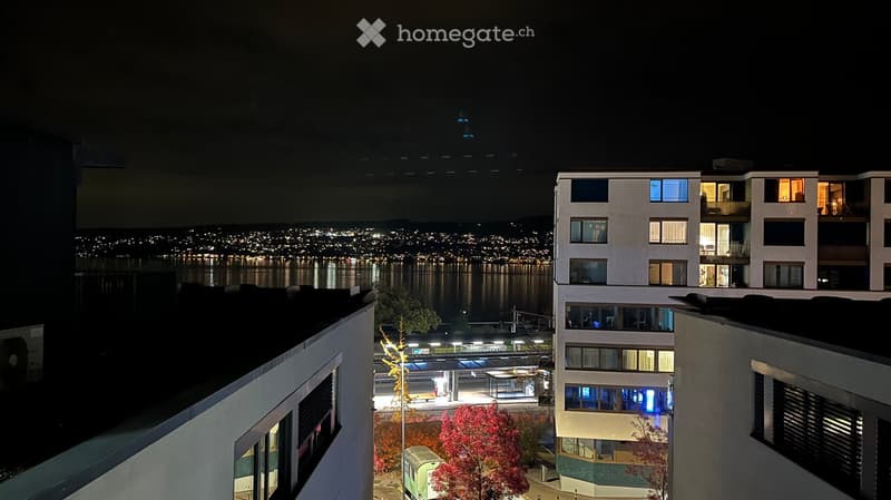 Night view of a modern apartment building with illuminated windows, overlooking a cityscape and waterfront.
