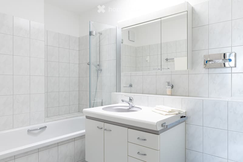 Modern bathroom with white tiles, a sink with a chrome faucet, a large mirror, a bathtub, and a glass-enclosed shower area.