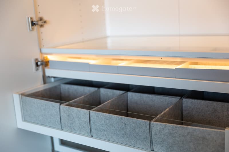 Modern kitchen with sleek, grey cabinets and multiple drawers, illuminated by soft lighting.