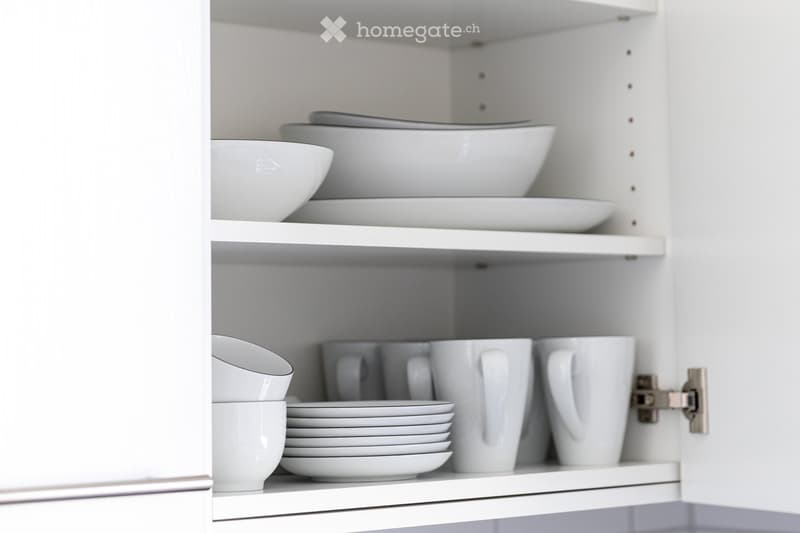 Open kitchen cabinet with neatly arranged white bowls, plates, and mugs on multiple shelves.