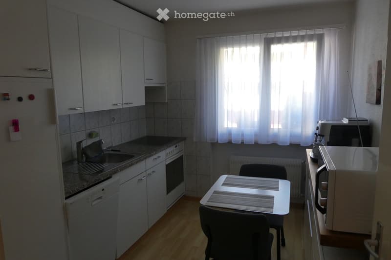 Modern kitchen with white cabinets, granite countertop, sink, oven, dishwasher, refrigerator, and a small dining area with a table and chairs.