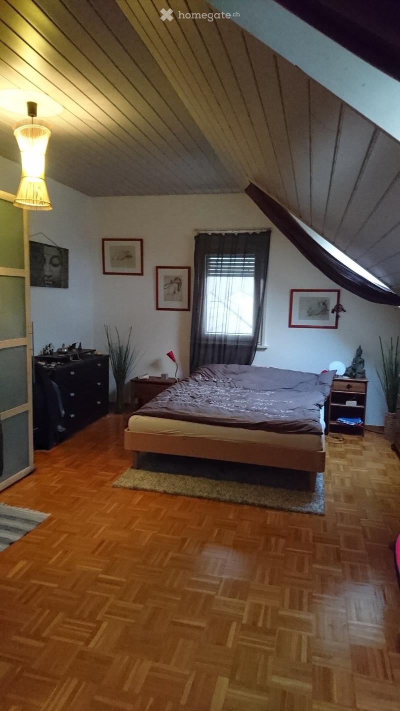 Cozy attic bedroom with wooden floors, slanted ceilings, and large window. Features a double bed, nightstands, lamp, and decorative elements.