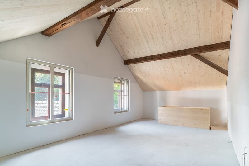Empty attic room with white walls, wooden beams, and skylight windows. The space features a slanted wooden ceiling and a small wooden platform in the corner.