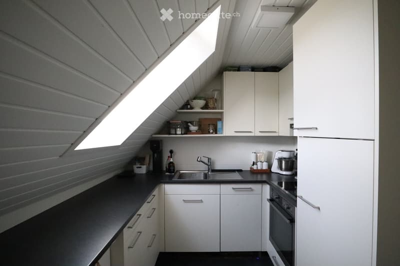 Modern kitchen with white cabinets, black countertops, and stainless steel appliances. Features include a sink, faucet, oven, refrigerator, coffee maker, and blender.
