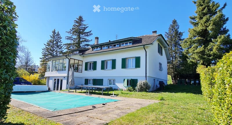 Two-story white house with green shutters, large windows, and a swimming pool in the front yard.