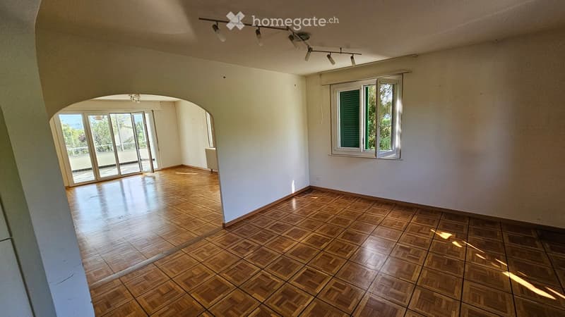 Empty room with wooden flooring, white walls, large windows, and a sliding glass door leading to a balcony.