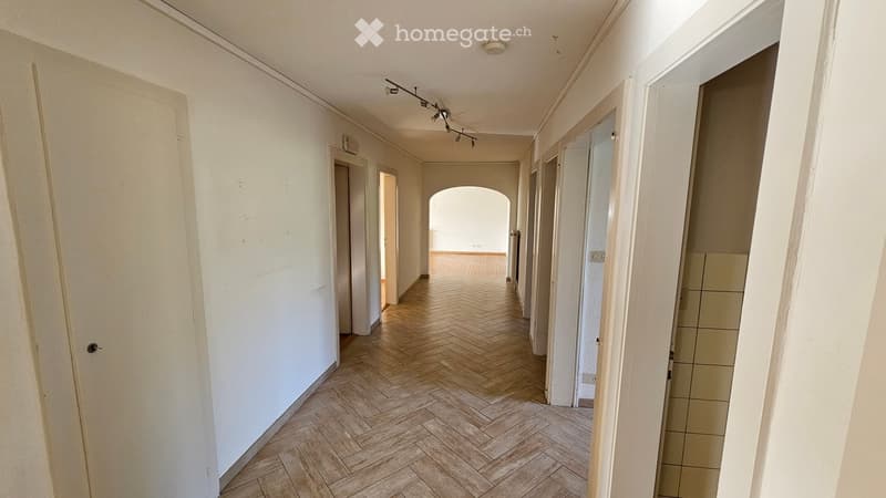 Empty hallway with wooden herringbone flooring, white walls, and several doors leading to other rooms.