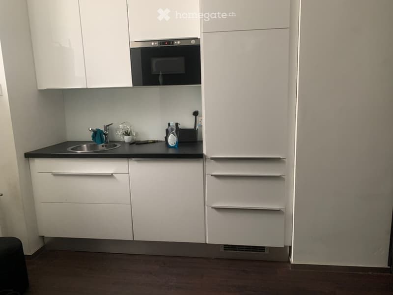 Modern kitchen with white cabinets, stainless steel sink, oven, and countertop items including a bottle and brush.