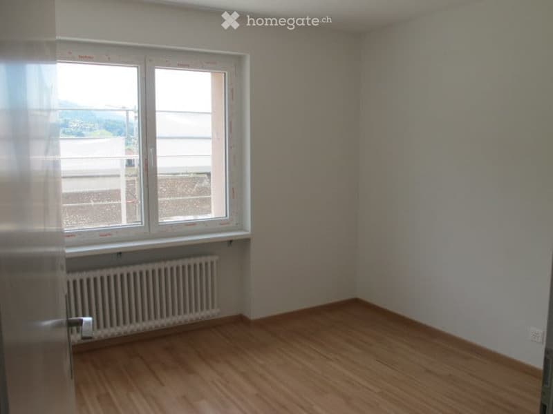 Empty room with wooden flooring, white walls, a window with blinds, and a radiator below the window.