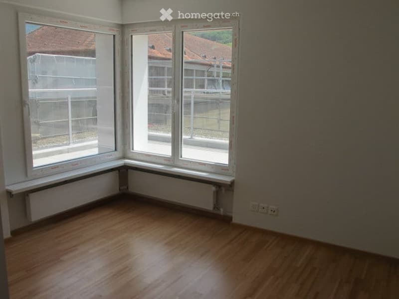 Empty room with wooden flooring, large windows, radiators, and electrical outlets.