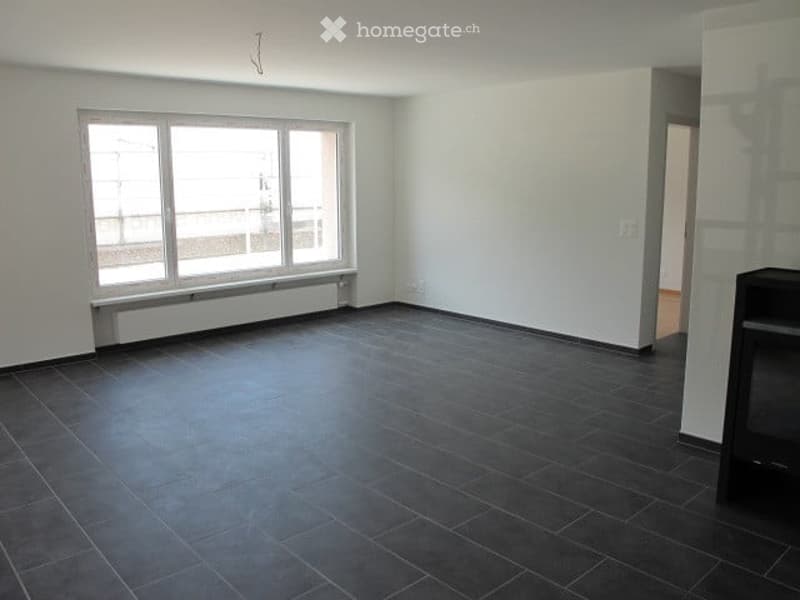 Empty room with dark tiled floor, white walls, large window with radiator below, and a doorway leading to another space.