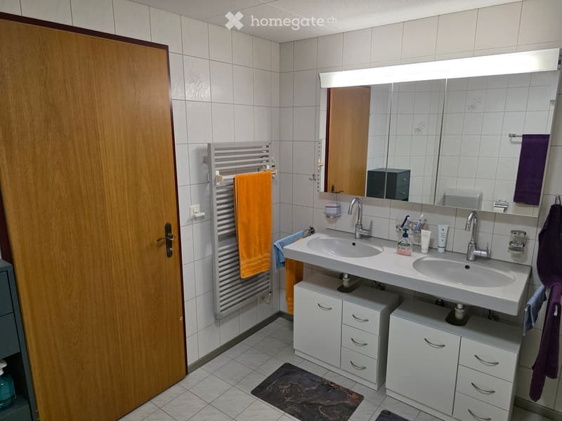 Modern bathroom with double sink, mirrored cabinet, towel radiator, and storage cabinets.