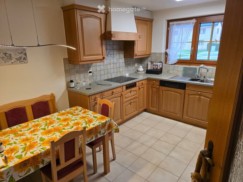 Bright kitchen with wooden cabinets, granite countertops, a dining area with a table and chairs, and a window with white curtains.