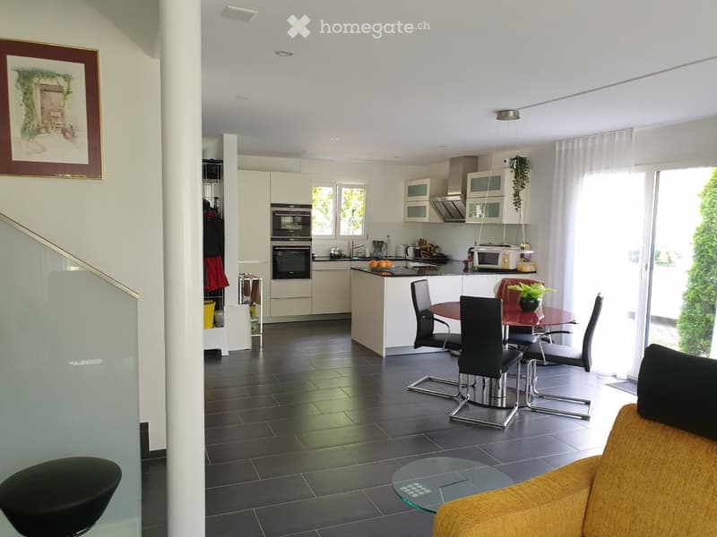 Modern open-plan living and dining area with a kitchen, featuring a yellow sofa, glass coffee table, dining table with chairs, and modern kitchen appliances.