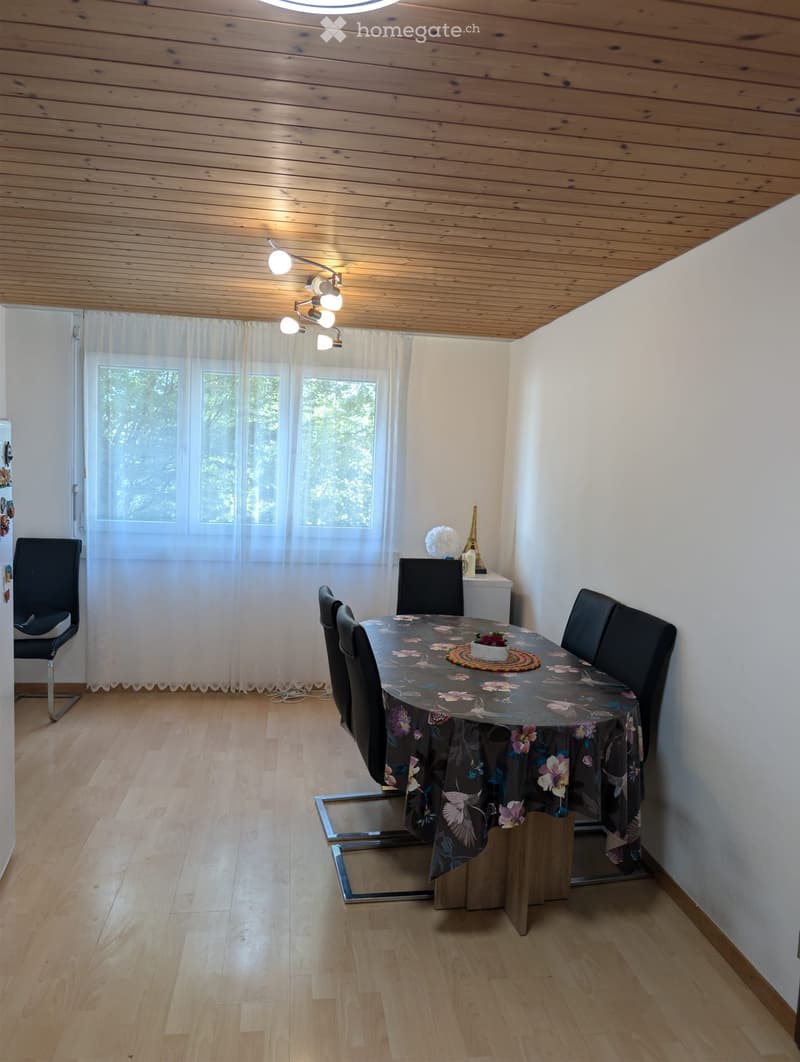Dining room with wooden floor, white walls, and a round dining table with a floral tablecloth and matching chairs.