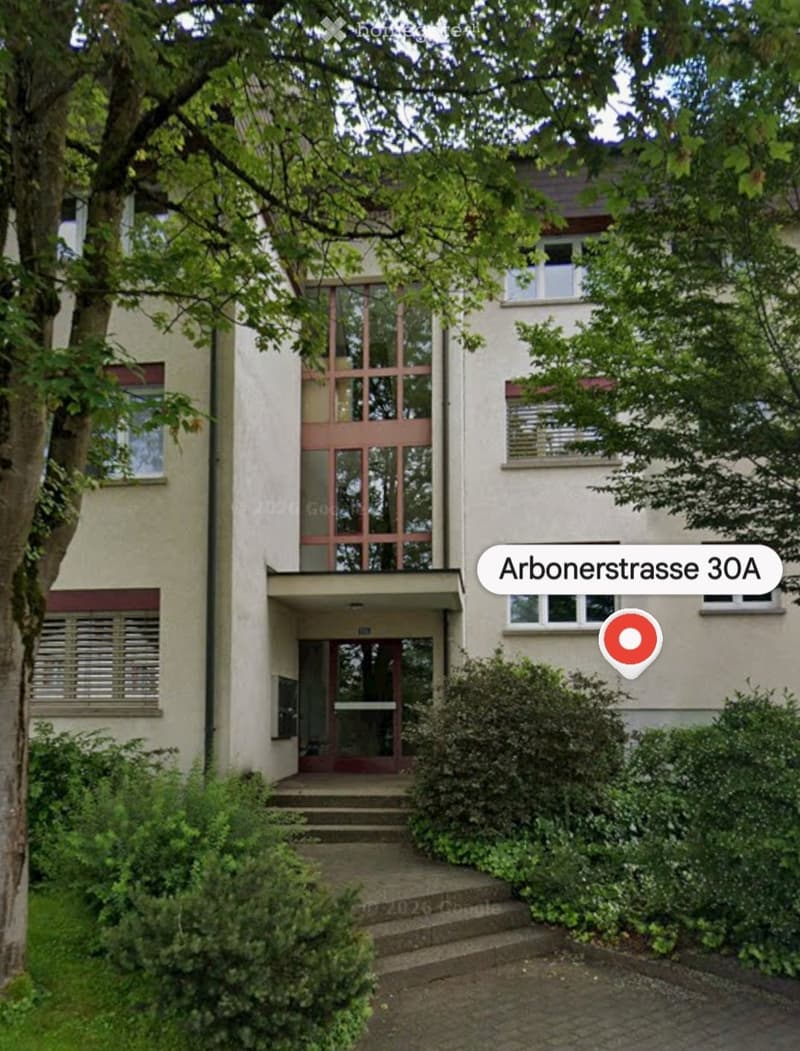 Two-story residential building with a modern facade, large windows, and a small entrance area with steps leading up to a glass door.