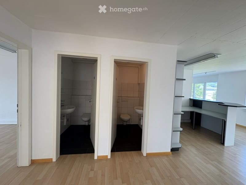 Empty room with wooden flooring, white walls, and two open doorways leading to bathrooms. The space is completely unfurnished with no visible furniture or equipment.