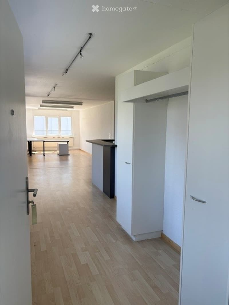 Empty room with wooden flooring, white walls, built-in closet, and a small desk area near the window.